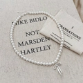 Detail of elegant pearl necklace featuring a silver bow pendant on a beige linen background - White