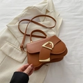 Braune Vintage-Satteltasche mit goldenem D-Verschluss auf einem beigen Blazer - Braun
