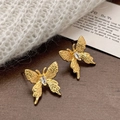 Boucles d'oreilles papillon dorées avec zircon et ailes texturées sur un fond de bois - Boucles d'Oreilles Papillon Zircon Doré
