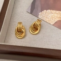 Detailed close-up of golden geometric multi-layer twisted knot earrings on beige fabric - Gold