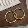 Orecchini a cerchio intrecciati dorati vintage con elegante trama metallica su legno - Oro