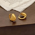 Detail van gouden druppeloorbellen met geborstelde textuur op rustieke stof - Goud