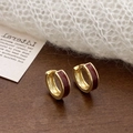 Dettaglio di orecchini huggie dorati con smalto rosso scuro su una superficie di legno - Rosso Ankle (Piccolo)