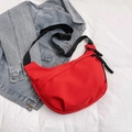 Minimalist red crescent crossbody bag with adjustable black strap on denim background - Red
