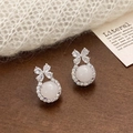 Detailed close-up of bow-knot chalcedony earrings with zircon inlay on a wooden desk - Silver White Resin