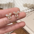 Elegantes pendientes de lazo dorado con microperlas y circón sobre fondo de punto suave - Pendientes de Botón de Perla con Lazo Dorados