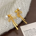 Boucles d'oreilles nœud doré avec perle blanche et pompon sur tissu blanc doux - Boucles d'Oreilles Nœud Doré Mat Perle Blanche