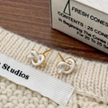 Close-up of golden knot earrings with white enamel finish on a soft knitted fabric - White Heart Earrings