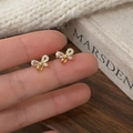 Detalle macro de pendientes de lazo dorado con circonitas sostenidos entre dedos - Dorado