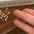 Vista macro de los pequeños pendientes de perlas sostenidos para escala y detalle - Dorado
