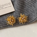 Macro detail of gold starburst earrings with sparkling zircon stones on textured fabric - Gold