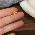 Macro shot of gold snowflake earrings with zircons held by hand over winter textiles - Snowflake Stud Earrings / Gold