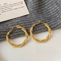 Detail von goldfarbenen gedrehten Creolen mit Glitzereffekt auf weißem Keramikteller - Gold