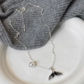 Elegante silberne Fischschwanz-Halskette mit weißer Perle auf einem Keramikteller - Schwarzer Fischschwanz