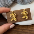 Detailed close-up of golden abstract flower earrings on a textured wooden card holder - Gold