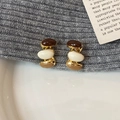 Dettaglio macro di orecchini smaltati a tre colori su maglieria e piatto di ceramica - Tonalità Tè al Latte
