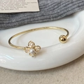 Elegant gold plated open bangle featuring a four-petal zircon flower and white pearl - Gold