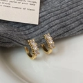 Elegante vergoldete Zirkonia-Ohrringe mit drei Kristallen auf grauem Stoffhintergrund - Gold