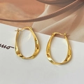 Primer plano de pendientes de aro ovalados trenzados dorados sobre un fondo minimalista - Dorado