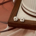 Minimalist silver twist knot earrings displayed on dark wood frame with vintage paper - Silver