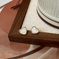 Vue macro de boucles d'oreilles cœur dorées avec texture nacre sur support en bois - Clous d'Oreilles Cœur Émail Blanc (A-1325)