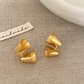Vue macro de boucles d'oreilles torsadées en or mat sur un fond de lin rustique - Or Mat