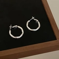 Close-up of silver hoop earrings with irregular hammered texture on a black display stand - Faceted Texture Style (A-1321)