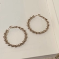 Dettaglio di grandi orecchini a cerchio dorati con texture martellata su sfondo libro - Grande Cerchio con Texture Increspata Oro (A-1201)