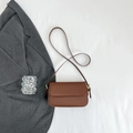 Détail d'un sac à bandoulière en cuir marron avec garnitures dorées sur fond blanc - Marron