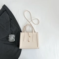 Flat lay of cream leather square crossbody bag with dual handles and shoulder strap - Off White