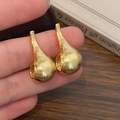 Detail of gold teardrop earrings with brushed metal texture held in hand near a book - Gold Earrings