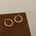 Close-up of wavy gold plated hoop earrings with textured finish on a dark wooden surface - Modern Wave Texture Style (A-1321)