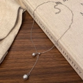 Detalle de collar en Y de plata con perlas grises sobre una portada de libro rústico - Plateado