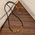 Dettaglio collana di perline nere sfaccettate con accenti dorati su legno scuro - Collana Cucita Oro e Nero