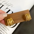Close-up of golden multi-layered wire wrapped C-shaped earrings held on wooden tray - Gold