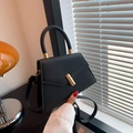 Fashionable black trapezoid handbag with golden cylindrical lock and top handle - Black