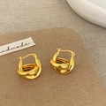 Dettaglio di orecchini a cerchio dorati con un design intrecciato lucido su sfondo di tessuto - Stile Nodo Intrecciato Irregolare / Oro