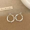 Detalle de pendientes de aro de plata con textura retorcida en tarjeta artesana - Plateado