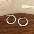 Dettaglio di orecchini a cerchio in argento con trama martellata unica e finitura irregolare - Argento