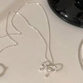 Dettaglio di una collana con ciondolo a fiocco argento su sfondo crema minimalista - Argento