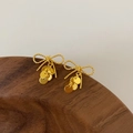 Detail of gold bow earrings with dangling sequins resting on a dark wooden bowl rim - Gold