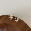 Close-up of silver bow earrings with shiny sequin tassels on a dark wood background - Silver