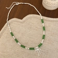 Detail of green beaded necklace with silver bow pendant on a rustic wooden background - Green Necklace