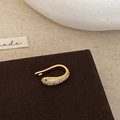 Macro view of gold-plated snake ear cuff with white zircons and emerald green gemstone - Gold