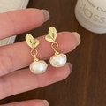 Detalle de elegantes pendientes de hoja dorada con perlas barrocas y textura fina - Dorado