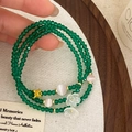 Detail eines mehrlagigen grünen Perlenarmbands mit goldenem Schmetterling und Blumen - Grasgrünes dreilagiges Armband