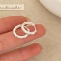 Dettaglio degli orecchini a cerchio in argento con trama a bambù tenuti in mano - Argento Opaco
