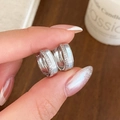 Detailed close-up of silver zircon hoop earrings with white inlay held by hand - Silver
