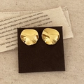 Detailweergave van onregelmatige gouden golf oorbellen op een bruine kaart in warm licht - Goud