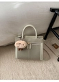 Detail of retro suede tote bag with plush charm on a textured beige rug setting - White With Pendant
